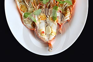 Top view, close up grilled fresh river shrimp with seafood sauce, slice garlic and mint leaves in white plate on black background