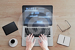 Top view and close up of man hands using laptop keyboard with glowing business chart hologram on screen at wooden desktop with