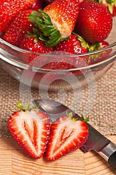 sliced, local, ripe and freshly picked strawberry, with pairing knife and a clear glass bowl of strawberries