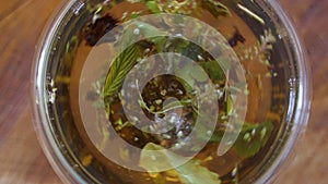 Top view close-up tea leaves opening in hot water at transparent cup. Brewing herbal green or black tea in mug at boiled