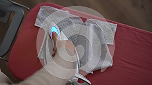 Top view. Close-up. An unrecognizable pregnant woman steams and irons a baby's loose jacket with a steam iron on an