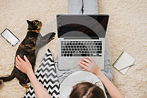 Top view close up of young girl sitting on floor using laptop computer typing studying working online, next lying small dark cat