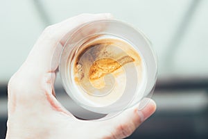 Top view and closeup of man& x27;s hand holding a glass of warm homemade latte coffee with froth, standing at balcony in the cold