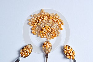 Top view closeup shot of a pile of corn kernels with three spoons also full of corn kernels