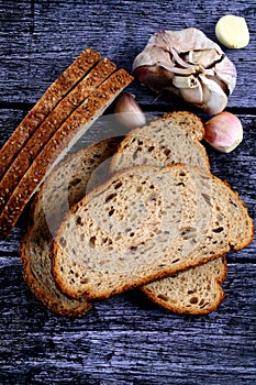 Top view closeup of a sliced loaf of brown bread and garlic cloves on a wooden table