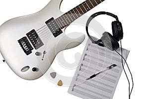 Top view of closeup of white electric guitar, two mediators, music paper for notes and guitar tabs, pen and headphones. Workspace