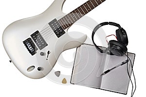 Top view of closeup of white electric guitar, two mediators, open notebook, pen and headphones. Workspace of musician. Isolated on