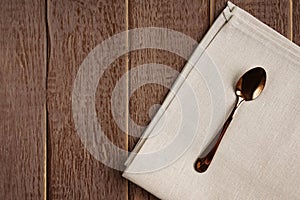 Top view of cloth napkin of beige color and served tea spoon on wooden table