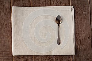 Top view of cloth napkin of beige color and served tea spoon on wooden table