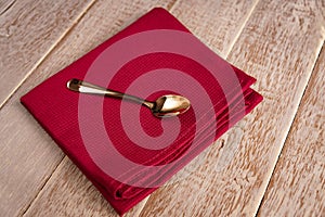 Top view of cloth napkin of beige color and served tea spoon on wooden table