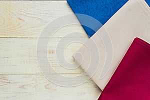 Top view of cloth napkins of beige, blue and burgundy colors on rustic white background