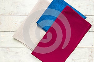 Top view of cloth napkins of beige, blue and burgundy colors on rustic white background