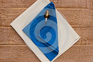 Top view of cloth napkins of beige, blue colors and served tea spoon on wooden table
