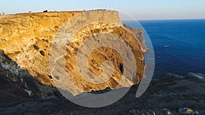 Top view of coastal cliff with blue sea at sunset. Shot. Beautiful view of golden sunset light on rocky cliffs of sea