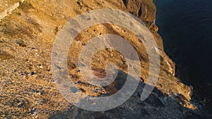 Top view of coastal cliff with blue sea at sunset. Shot. Beautiful view of golden sunset light on rocky cliffs of sea