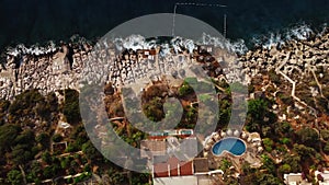 Top view of a coastal resort with lounge zone and swimming pool located in front of rocky beach