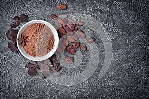Top view of cocoa powder in white bowl with chunks of chocolate and whole cocoa beans