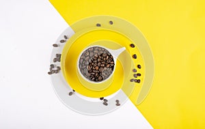 Top view of coffee cup full of beans on yellow and white background