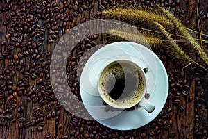 Top view of coffee cup on saucer with grass flowers and roasted coffee beans on wooden table