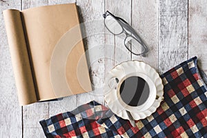 Top view of Coffee cup with tablecloth, notebook and glasses on wooden table background.