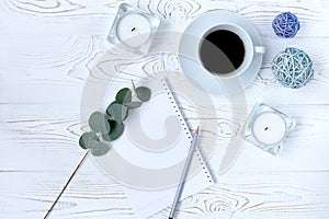 Top view of coffee mug, blank notepad, pencil, flowers and candles on white table. Flat lay