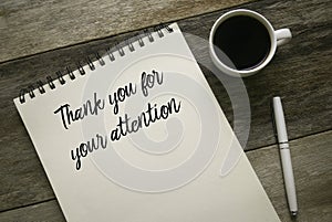 Top view of coffee,pen and notebook written with statement of Thank you for your attention on wooden background