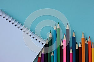 Top view of colored pencils and notebook on blue background. Back to school concept