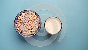 top view of colorful cereal corn flakes in a bowl and glass of milk on blue