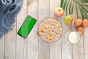 top view of colorful cereal corn flakes in a bowl and smart phone on table