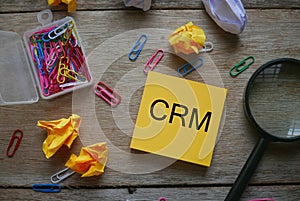 Top view of colorful paper clips magnifying glass,trash paper and yellow sticky note written with CRM & x28;Customer Relationship