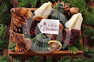 Top view of colorful paper ornaments in various shapes and a label with Christmas greeting text in wooden box