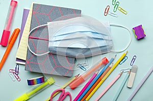 Top view of colorful pencils, pens, scissors, notepads and facial mask for protection.Concept of back to school and pandemic situa