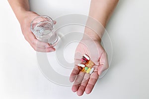 Top view of Colorful pills, capsule medicines and glass of water in man`s hands. Treating COVID-19 at home on the doctor`s