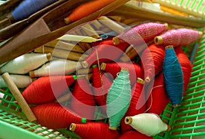 Top view colorful yarns on spool and empty wooden spools in plastic basket. Yarns in weaving shuttle tool. Textile fabric weave