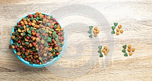 Top view Colourful Dried dog food in blue bowl on wood table background and Dog or cat paw print. Grain animal pet food banner