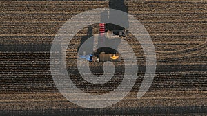 Top view of combine loading off ripe corn grains into tractor trailer. Aerial shot of farmland during harvesting process