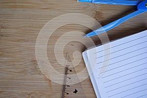 Top view of a compass with an open notebook and a ruler on a wooden surface