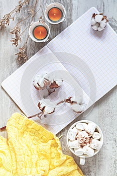Top view composition with cup of coffee and marshmallow, candles, cotton plant flower branches, notepad and copy space. Autumn