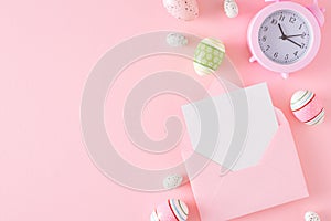 Top view composition made of colorful eggs, envelope with letter, alarm clock on pastel pink background