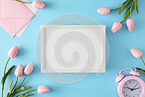 Top view composition made of envelope, spring flowers, pink alarm clock and white frame in the middle