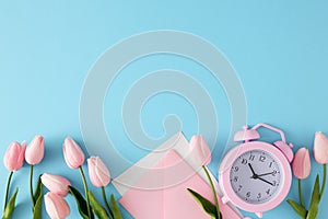 Top view composition made of envelopes, spring flowers and pink alarm clock on blue background