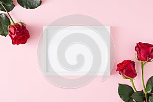 Top view composition made of red roses on pastel pink background and white frame