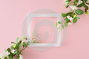 Top view composition made of spring flowers and white frame in the middle on pastel pink background.