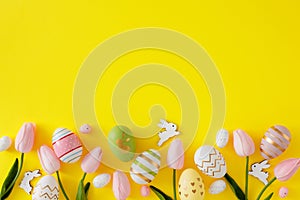 Top view composition made of spring tulips, color eggs and cute easter bunnies on yellow background