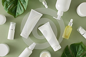 Top view composition made of white cream tubes, dropper bottles, cream jars and tropical leaves