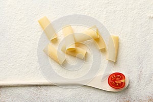 Top view composition with raw Italian pasta- tortiglioni- and a small tomato on a wooden spoon on a white floured background with