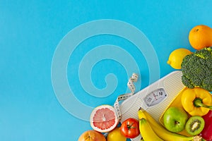 Top view composition of scales and tape measure, plate with fruits and vegetables on blue background