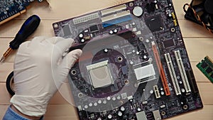 Top view computer technician installing RAM on motherboard at wooden desk with tools and electronic components