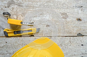 Top view construction tools such as a yellow hard hat, spirit level, measuring tape, folding ruler arrayed against a wooden plank