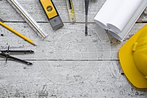 Top view construction tools such as a yellow hard hat, spirit level, measuring tape, folding ruler arrayed against a wooden plank